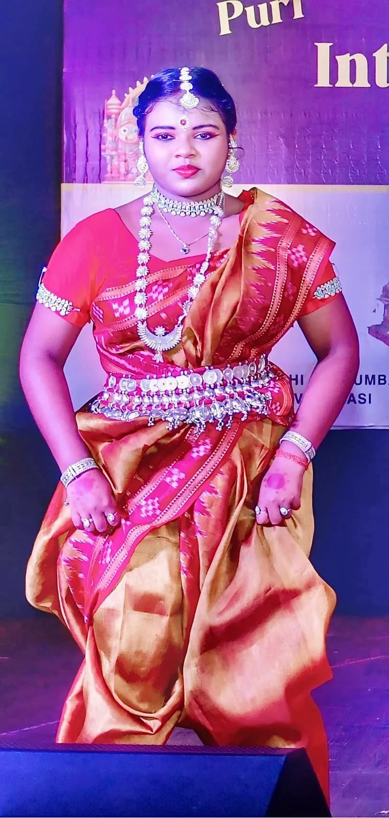A solo dancer in an orange and red costume on stage under blue light