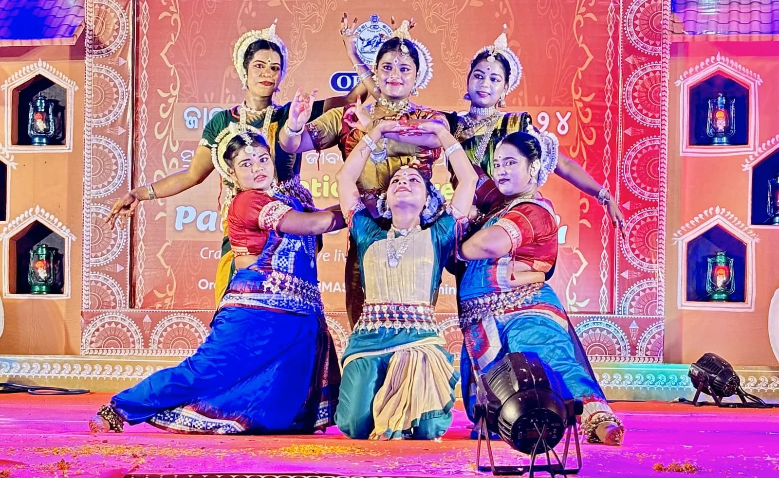 Six dancers holding a sculptural group pose on stage